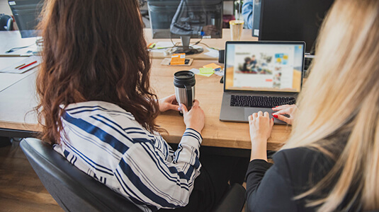 Two businesswomen navigating through their business website - checking the efficacy of their landing pages.